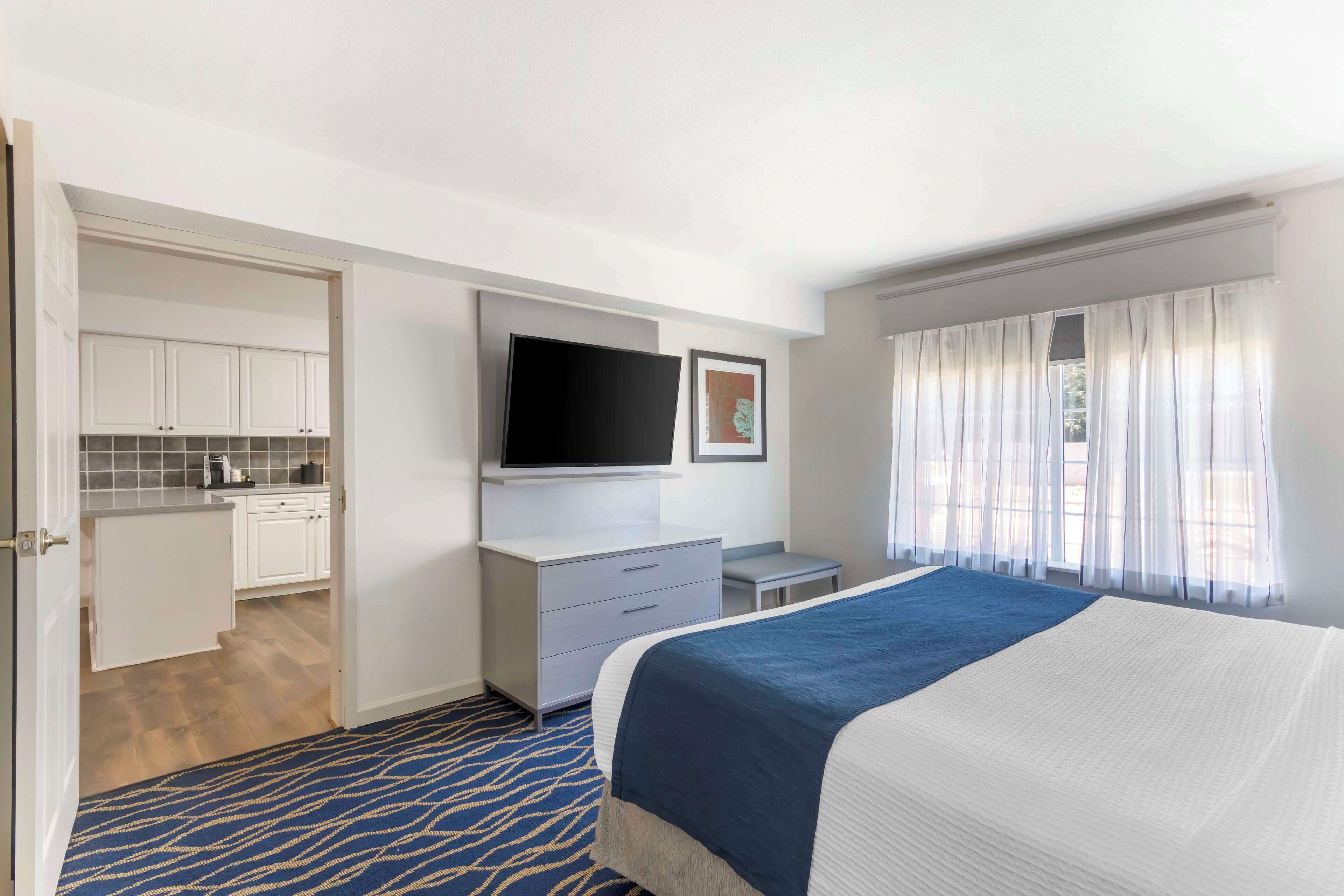 A hotel room with a bed, a TV, a desk, and a kitchenette.