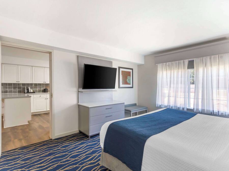 A hotel room with a bed, a TV, a desk, and a kitchenette.