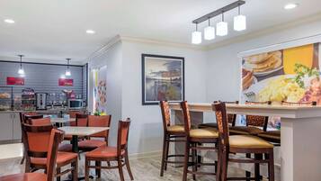 Un comedor moderno con sillas y mesas de madera, una zona de cocina con electrodomésticos y un cuadro grande en la pared.