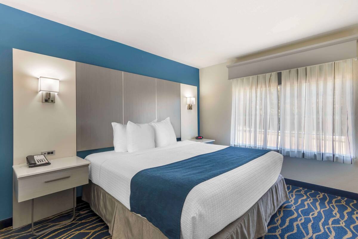 Een hotelkamer met een bed, nachtkastjes, een telefoon en een raam met gordijnen.