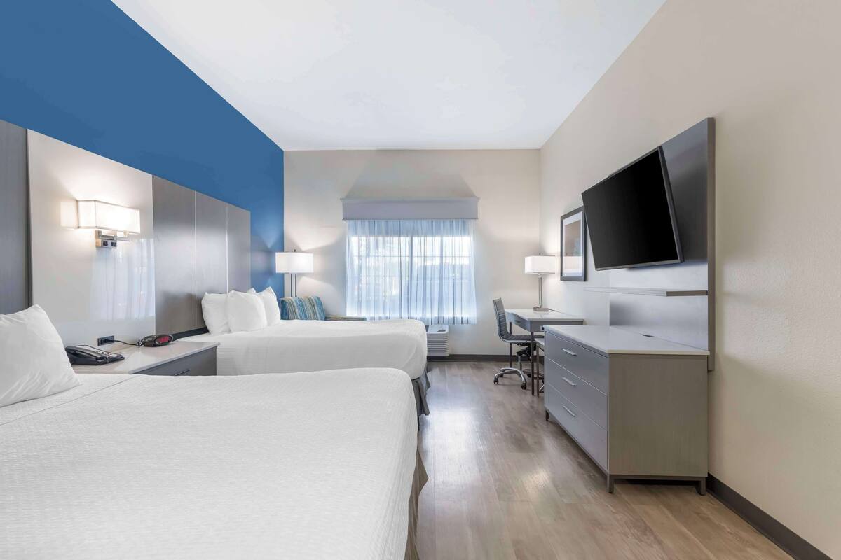 Een hotelkamer met twee bedden, een bureau, een stoel, een televisie en een groot raam met gordijnen.