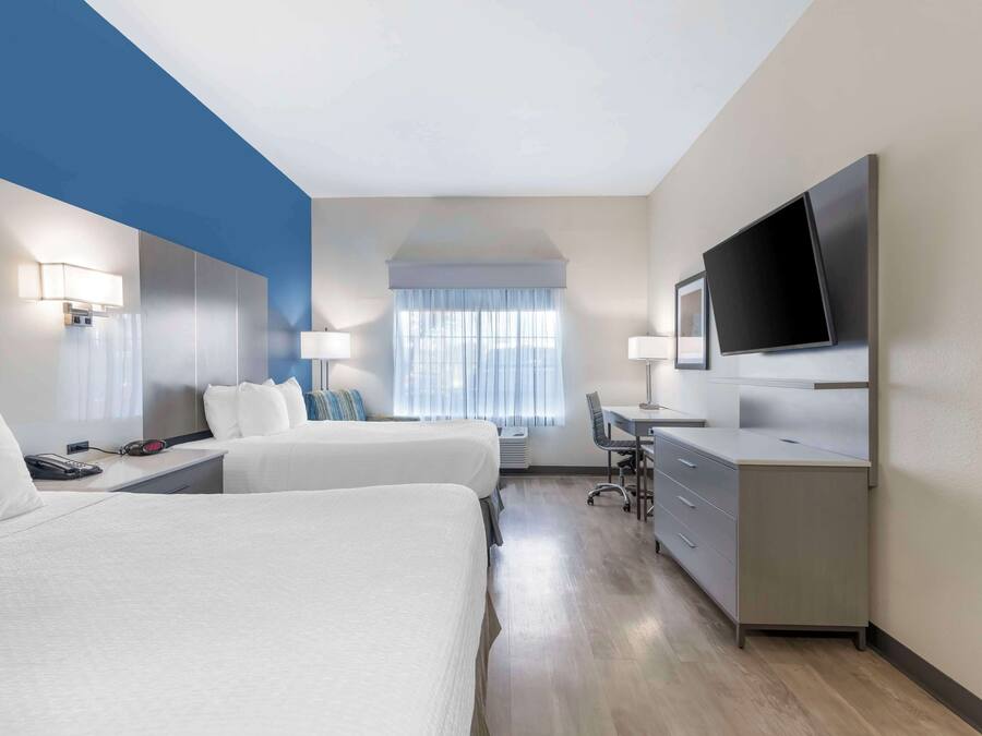 A hotel room with two beds, a desk, a chair, a TV, and a large window with curtains.