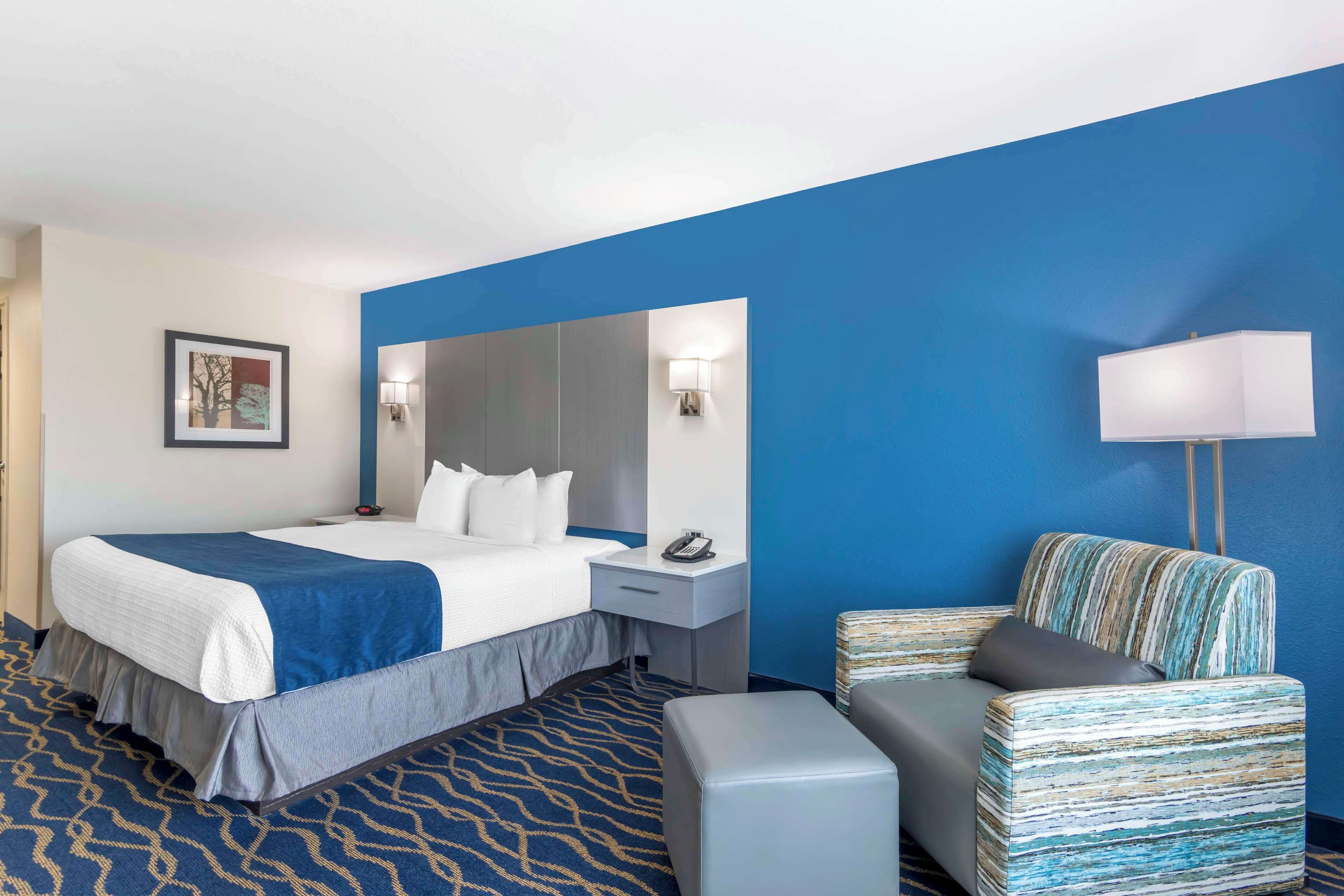 A hotel room with a bed, bedside table, lamp, and a striped armchair.