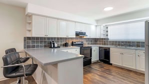 Una cocina moderna con gabinetes blancos, horno empotrado, lavavajillas y una zona de bar con dos taburetes negros.