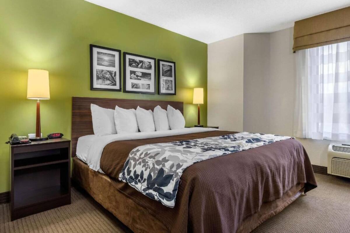 A hotel room with a bed, two bedside lamps, a nightstand, and a wall with three framed pictures.