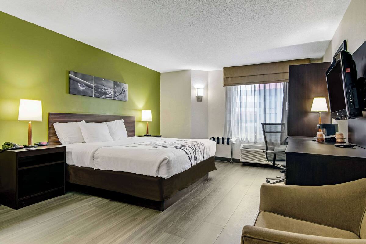 A hotel room with a bed, bedside lamps, a desk with a TV, and a chair.
