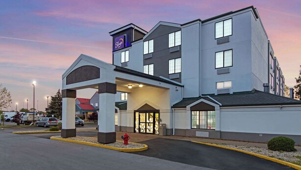 A modern hotel with a prominent entrance, a covered waiting area, and a parking lot. - Sleep Inn near I-80 and I-94 (Lansing)