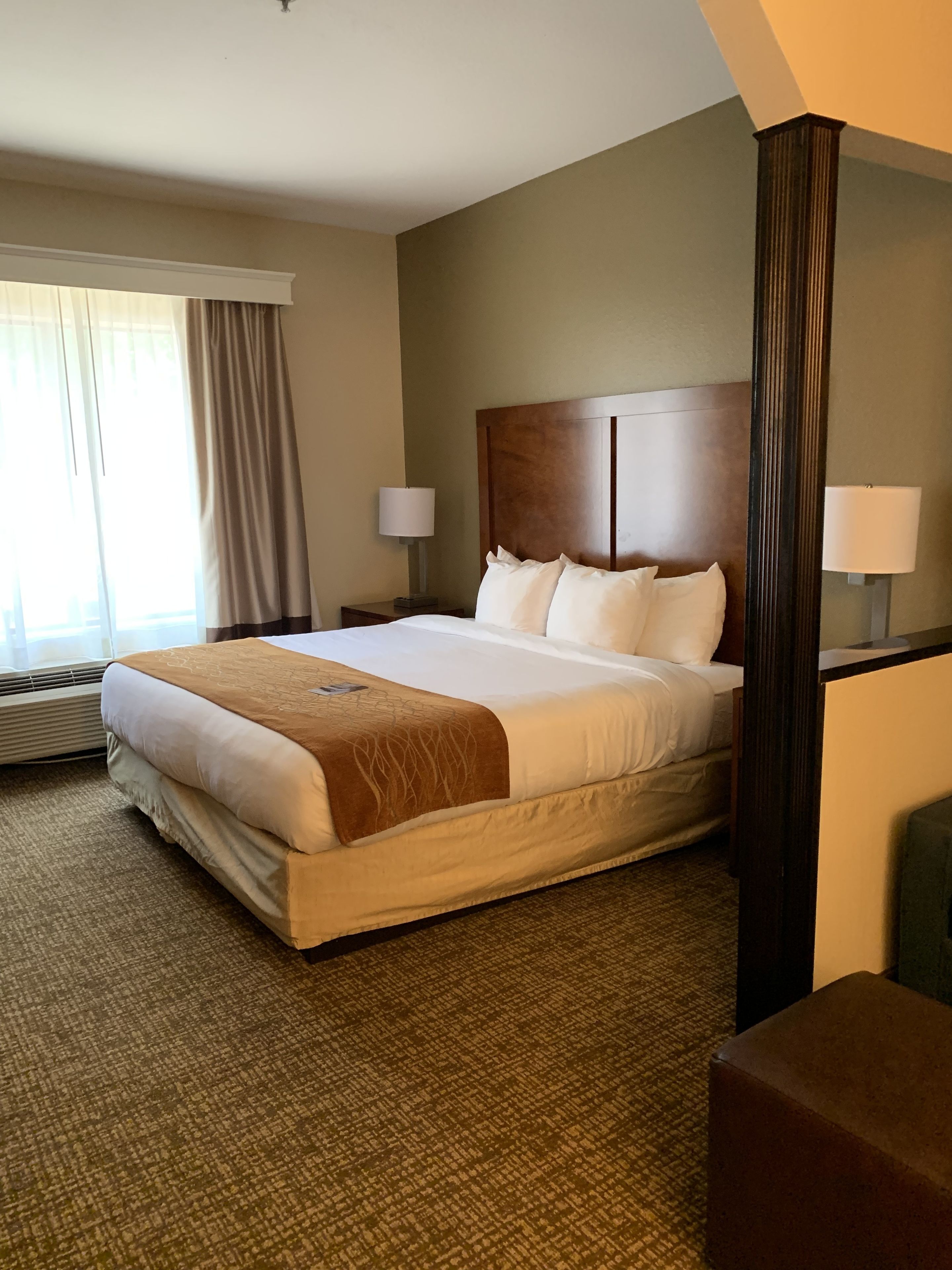 A hotel room with a large bed, two bedside lamps, a headboard, and a window with curtains.
