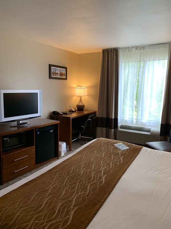 A hotel room with a bed, a desk with a computer, a television, and a window with curtains.