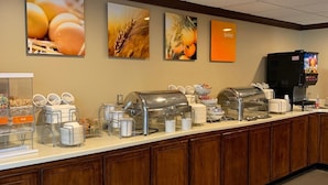 Ein Frühstücksbuffet mit verschiedenen Speisen, einer Kaffeemaschine und einem Fernsehbildschirm, der ein Programm zeigt.