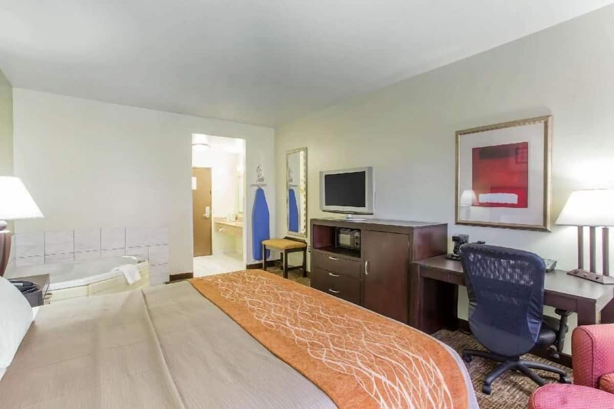 A hotel room with a bed, desk, chair, television, and a bathroom visible through an open door.