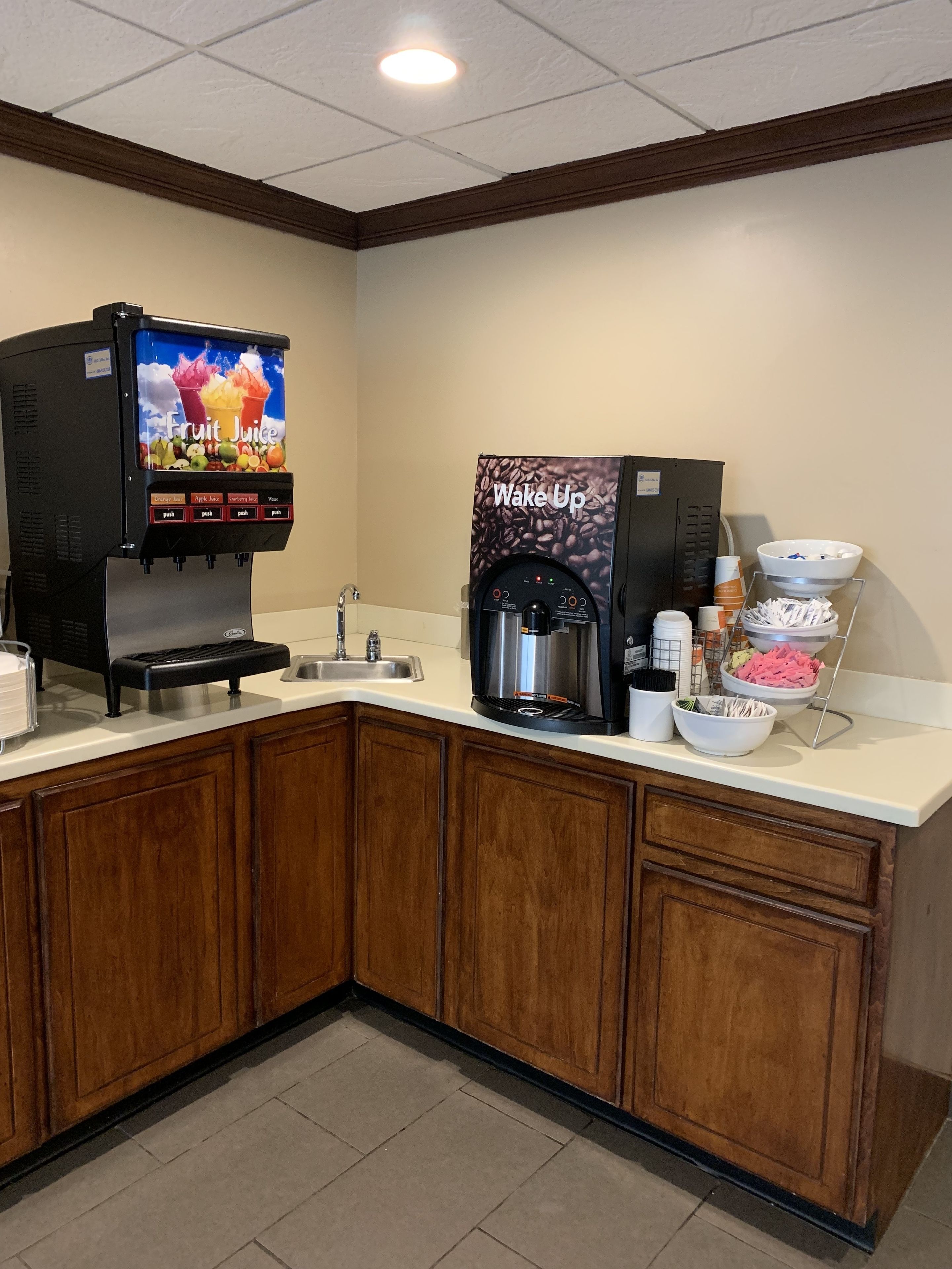 Una cocina con dispensador de zumo, máquina de café y un bol de fruta.