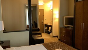 Ein Hotelzimmer mit Bett, Schreibtisch, Fernseher, Kleiderschrank und einem durch eine offene Tür einsehbarer Badezimmer.