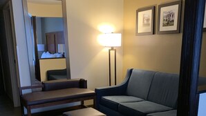 A hotel room with a sofa, ottoman, a standing lamp, a mirror, and framed pictures on the wall.