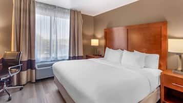 Une chambre d’hôtel avec un grand lit, un bureau, une chaise, une table de chevet et une fenêtre avec des rideaux.
