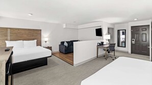 A modern hotel room with a large bed, a desk with a chair, a sofa, and a TV mounted on the wall.