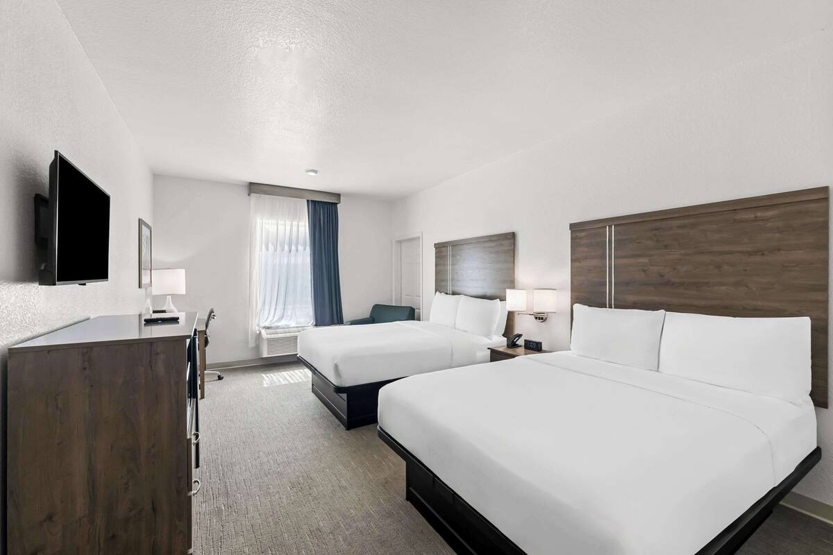 A hotel room with two beds, a desk, a TV, and a window with curtains.
