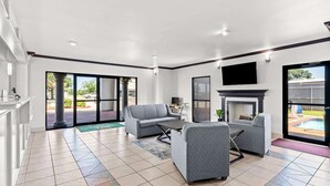 A spacious living area with a fireplace, grey sofas, and a large window overlooking a pool.