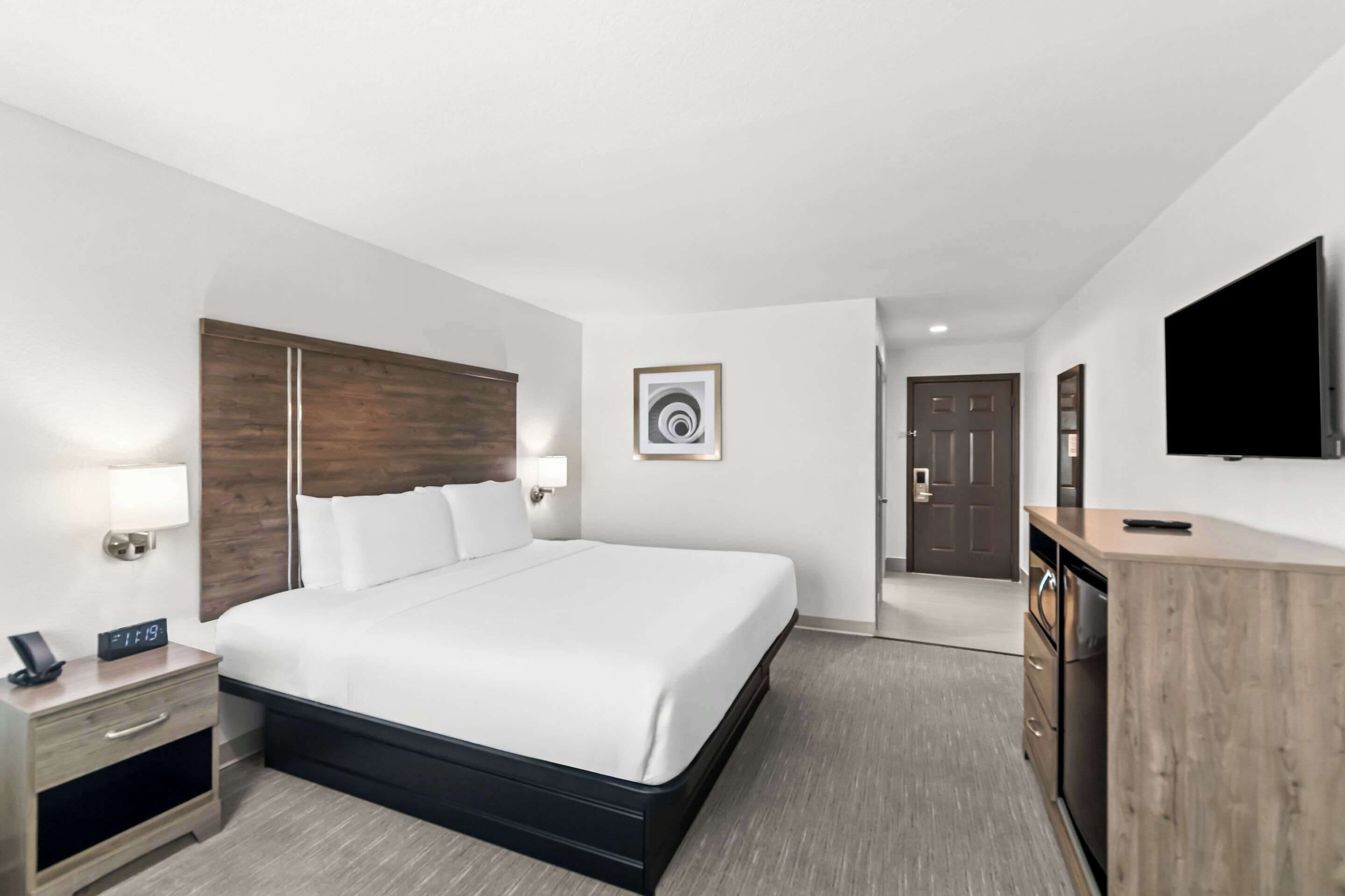 A hotel room with a large bed, bedside tables, a TV, and a wooden dresser.