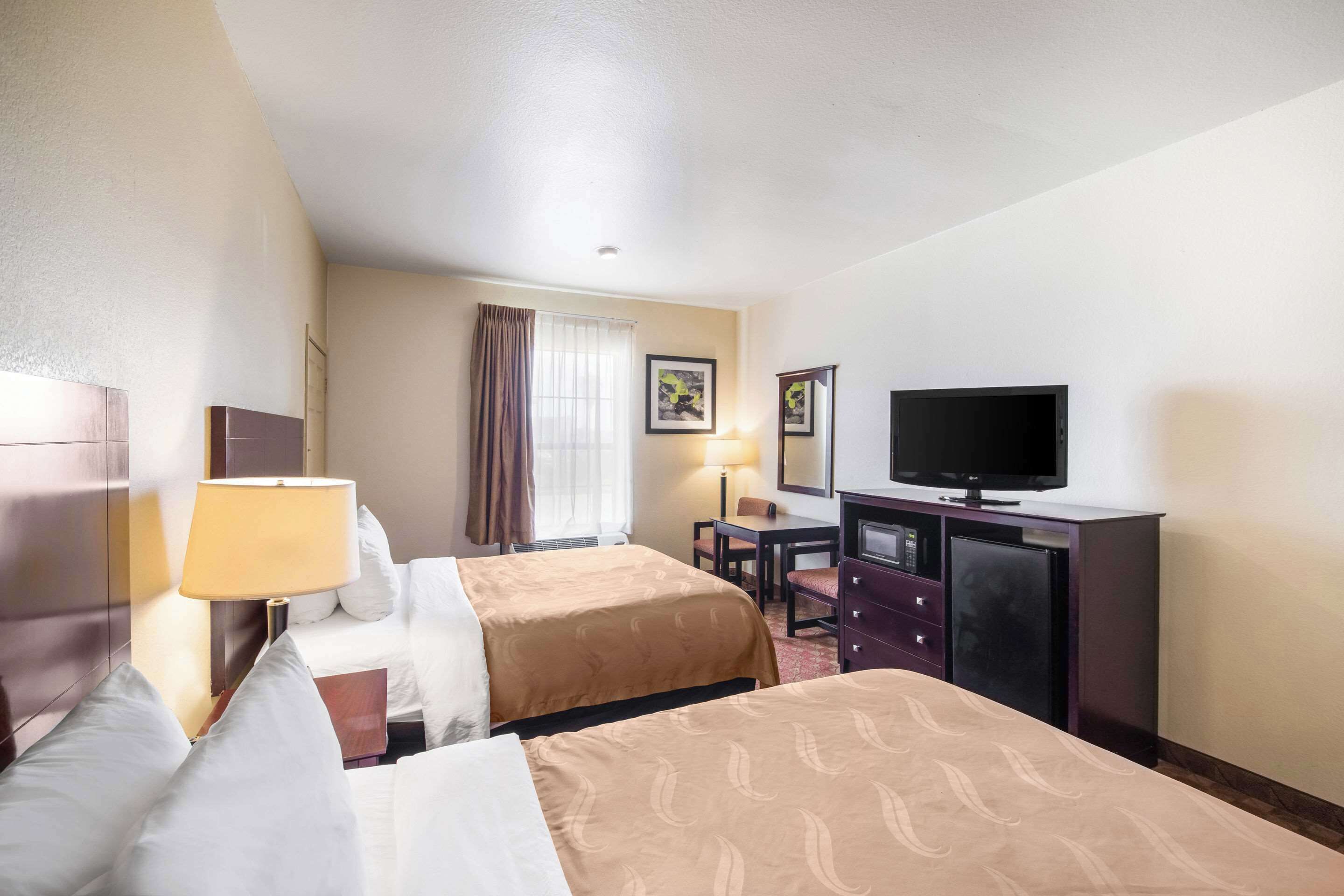 A hotel room with two beds, a desk, a television, and a dresser.