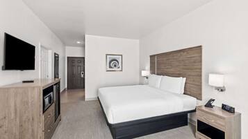 Una camera d'albergo con un letto grande, una TV, una scrivania con una lampada e un comodino con una sveglia.