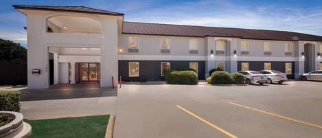 A modern hotel with a two-story structure, a covered entrance, and a parking lot with several cars.