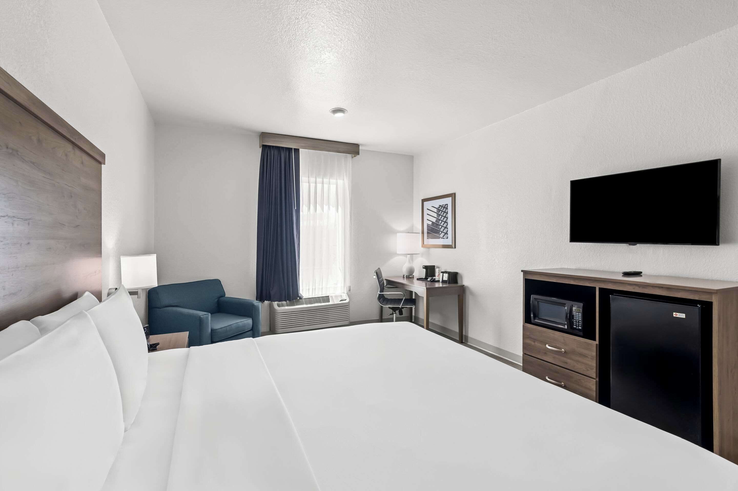 A hotel room with a large bed, a desk with a computer, a television, and a microwave.