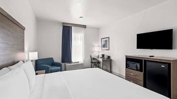 Ein Hotelzimmer mit einem großen Bett, einem Schreibtisch mit Computer, einem Fernseher und einer Mikrowelle.