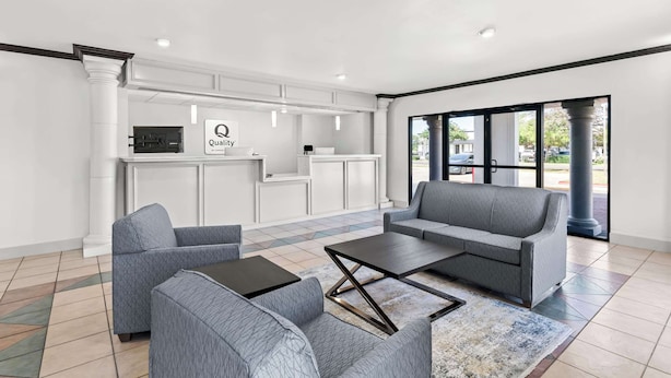 A modern lobby with grey sofas, a coffee table, and a reception desk with a sign reading "Quality."