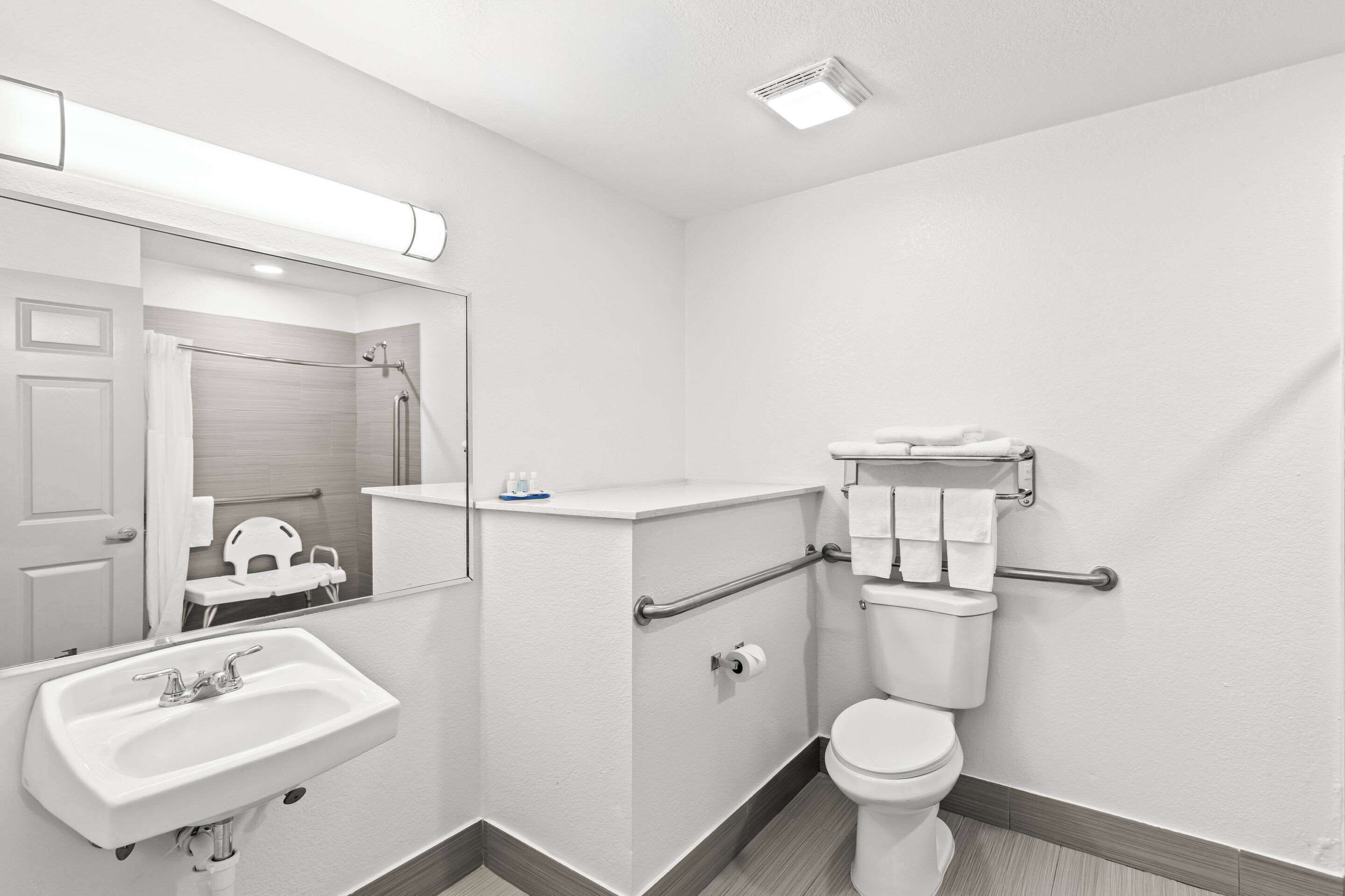 A modern bathroom with a white sink, toilet, and handrails.
