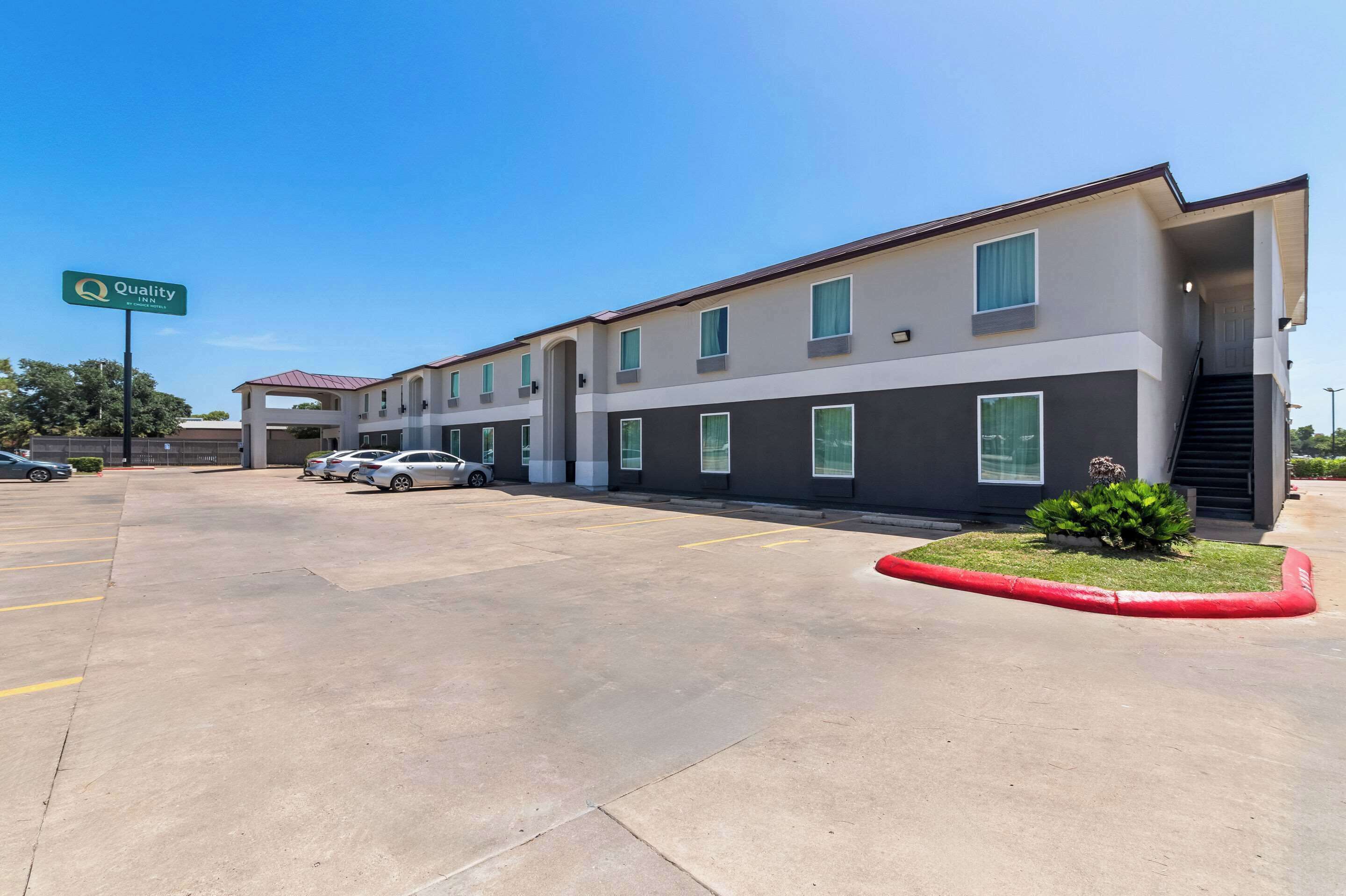 A Quality Inn hotel with a modern design, featuring a parking lot with several cars and a well-maintained lawn area.