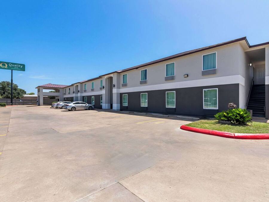 A Quality Inn hotel with a modern design, featuring a parking lot with several cars and a well-maintained lawn area.