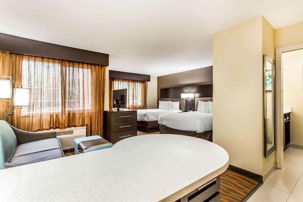 Une chambre d’hôtel comprenant un lit, un bureau, une chaise, une commode et une fenêtre avec des rideaux.