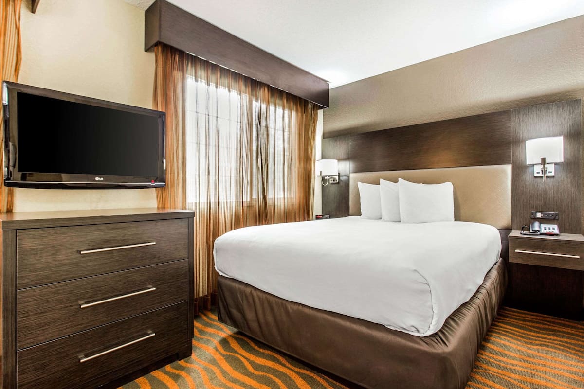 Una habitación de hotel con una cama grande, un televisor de pantalla plana, un aparador y una mesita de noche con lámpara.