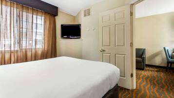 A hotel room with a large bed, a television mounted on the wall, a door, and a chair.