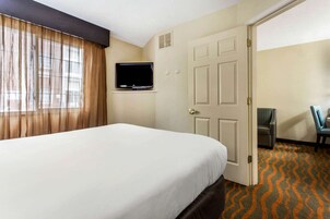A hotel room with a large bed, a television mounted on the wall, a door, and a chair.