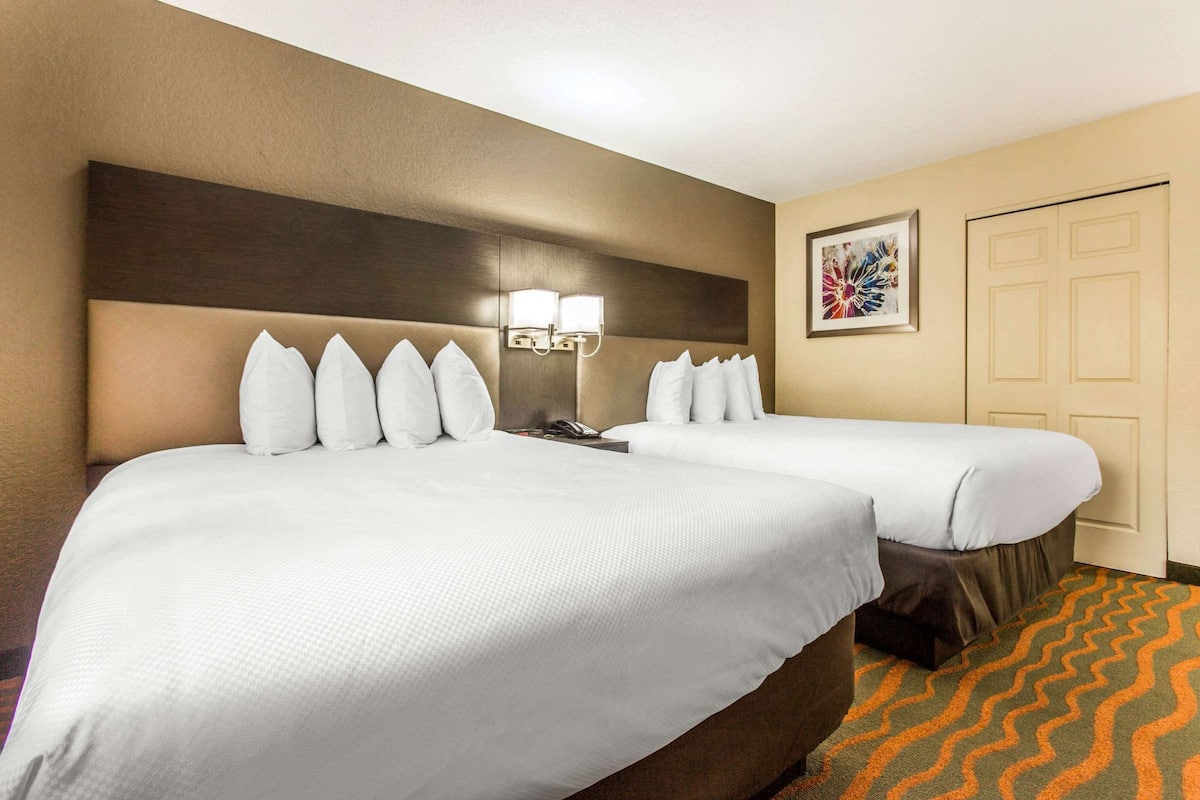 Habitación de hotel con dos camas, cabecero con lámpara, teléfono e imagen enmarcada en la pared.