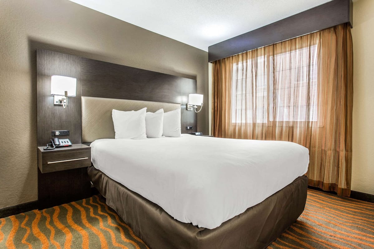 Una habitación de hotel con una cama grande, dos mesitas de noche con lámparas, un teléfono y una ventana con cortinas.