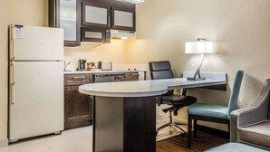 Cocina pequeña equipada con refrigerador, microondas y estufa. Hay una mesa de comedor con dos sillas y una lámpara.