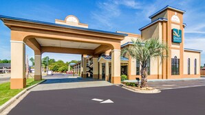 A hotel entrance with a covered walkway, palm trees, and a clear sky. - Quality Inn & Suites Lake City (Lake City)
