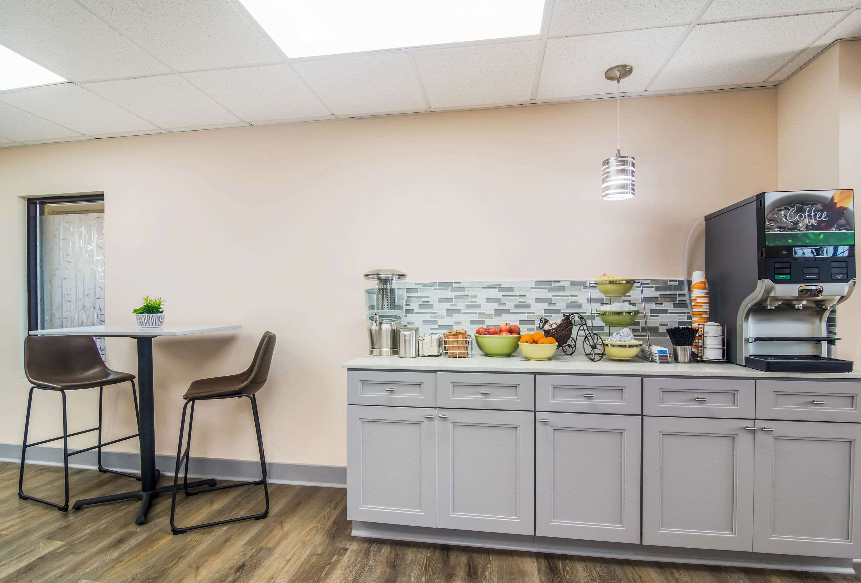 A kitchenette with a coffee machine, two bar stools, a small table, and a tiled backsplash.
