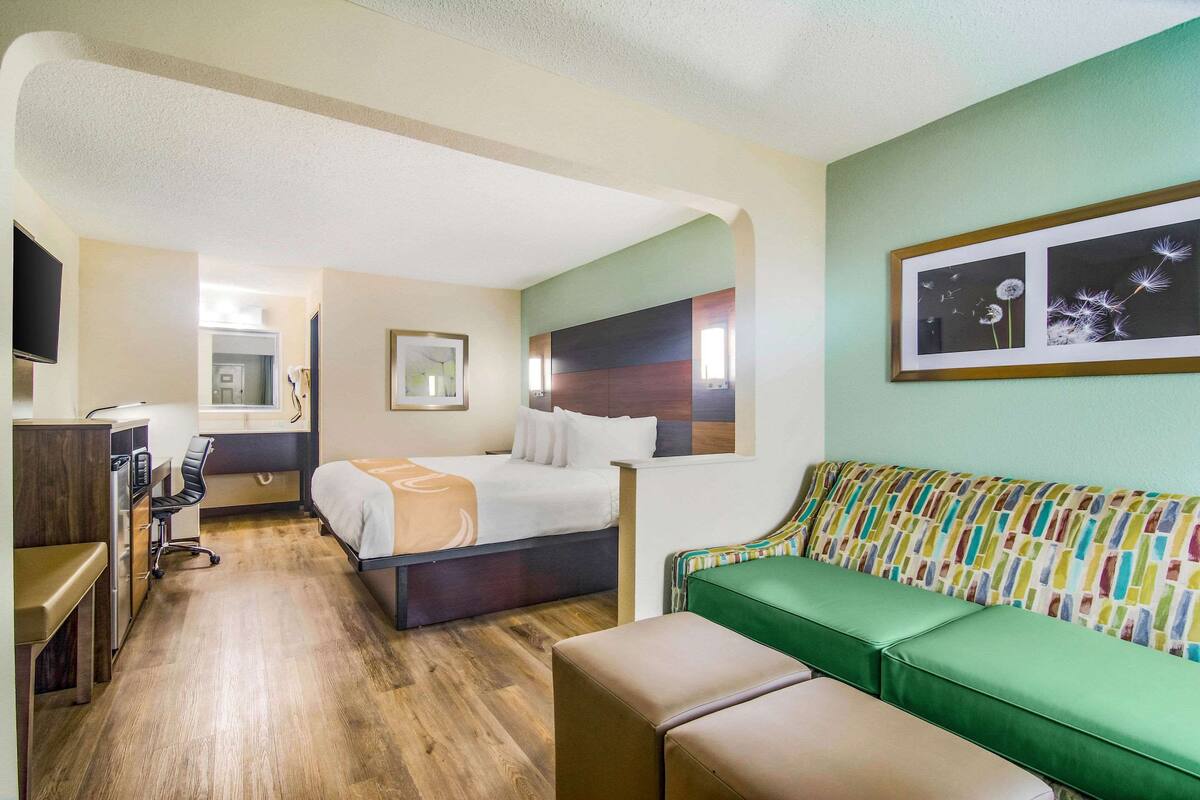 A hotel room with a bed, desk, chair, and a green sofa.