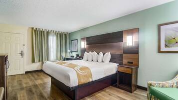 Una habitación de hotel con una cama grande, un cabecero de madera, una mesita de noche, un sillón verde y una puerta.