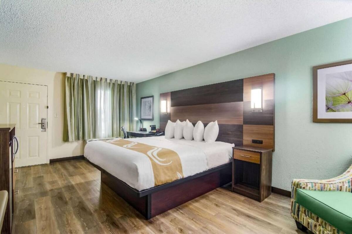 A hotel room with a bed, bedside table, and a chair.