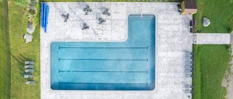 An aerial view of a swimming pool with multiple lanes, surrounded by lounge chairs and a covered seating area.