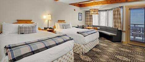 A hotel room with two beds, a large window with curtains, a patterned carpet, and wooden beams on the ceiling.