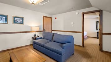 Una habitación con un sofá azul, una mesa de madera, cuadros enmarcados en la pared y una puerta que da a otra habitación.