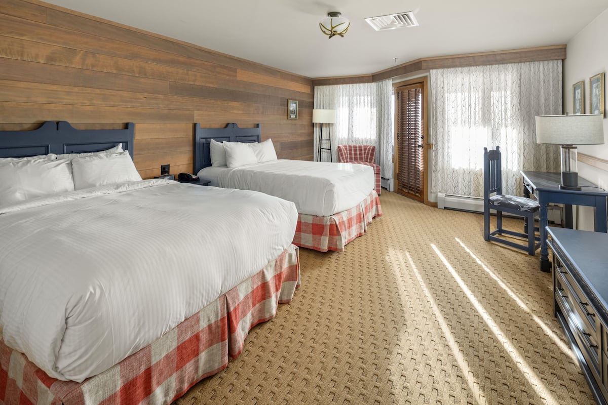 Habitación de hotel con dos camas, un escritorio, una silla y una ventana con cortinas.