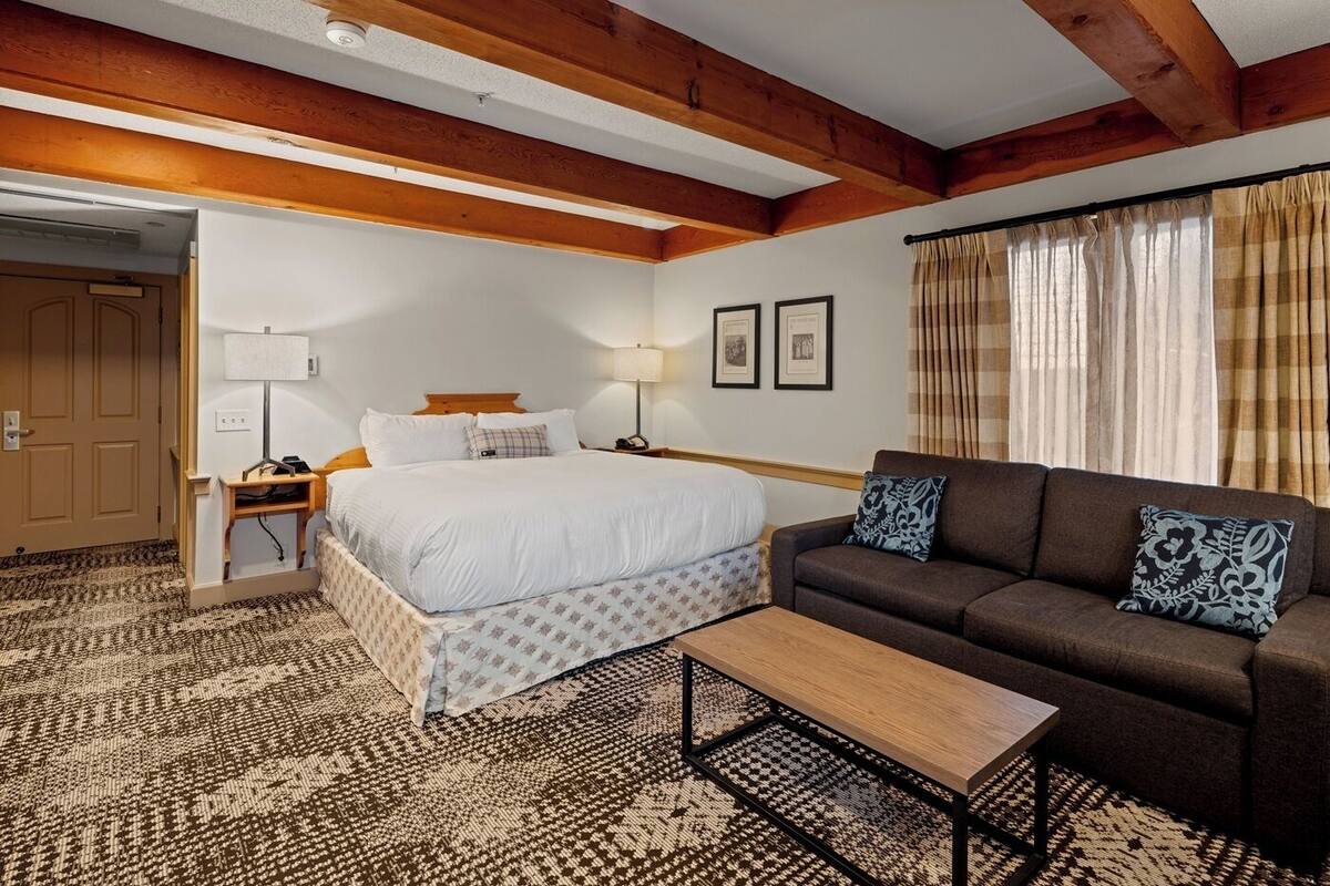 Una habitación de hotel con cama, sofá, mesita de centro, mesita de noche, lámpara y puerta.