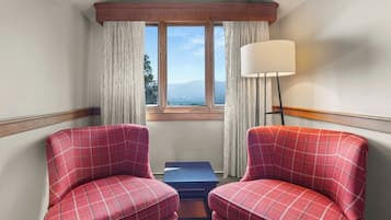 Habitación de esquina con dos sillones a cuadros, una mesita, una lámpara y una ventana con cortinas.